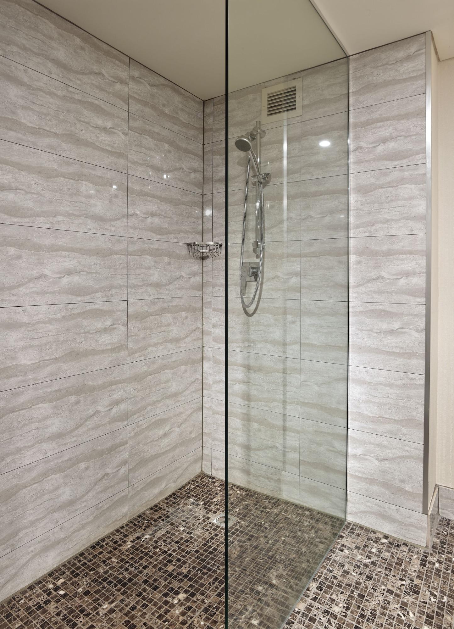 Stamford Grand Adelaide Hotel Glenelg Exterior photo The photo shows a modern shower enclosure with a transparent glass door. The interior features tiled walls in a light, marble-like pattern, creating a clean and sleek look. There is a showerhead mounted on the wall, and the floor appears to be tiled 