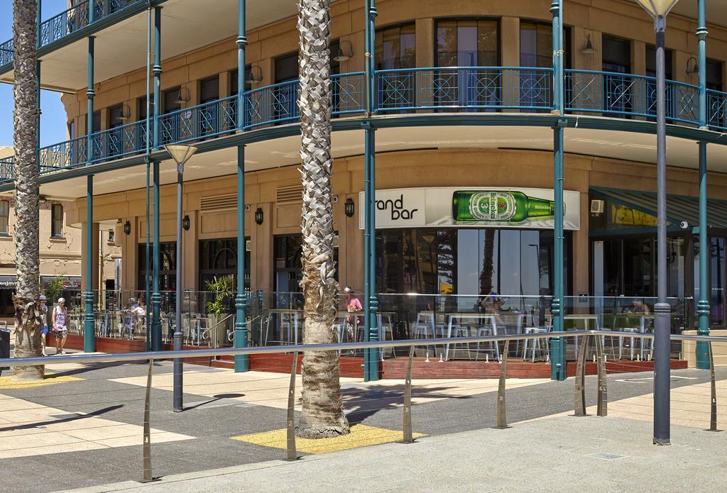 Stamford Grand Adelaide Hotel Glenelg Exterior photo The photo shows a corner of a building that houses a bar with the name "End Bar" prominently displayed. It's a multi-level structure with balconies featuring decorative railings. In front of the bar, there are tables and chairs, indicating a dining o