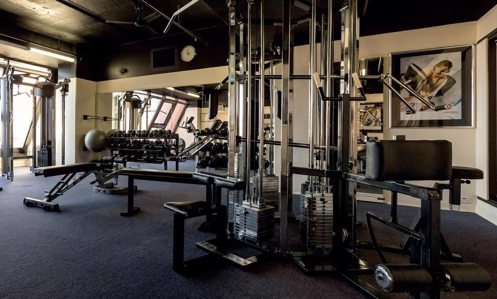 Stamford Grand Adelaide Hotel Glenelg Exterior photo The photo shows a gym interior with several pieces of exercise equipment. In the foreground, there is a multi-station machine that features various pulleys and weights. To the side, there are benches and free weights, including dumbbells. The gym has