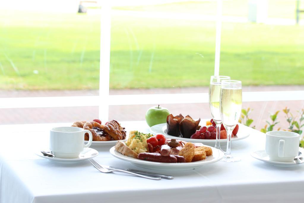 Stamford Grand Adelaide Hotel Glenelg Exterior photo The photo displays a beautifully arranged breakfast setup on a white tablecloth. In the center, there is a large white plate with a variety of foods, including eggs, sausage, and fresh fruit. Surrounding the plate are a few other food items, such as 